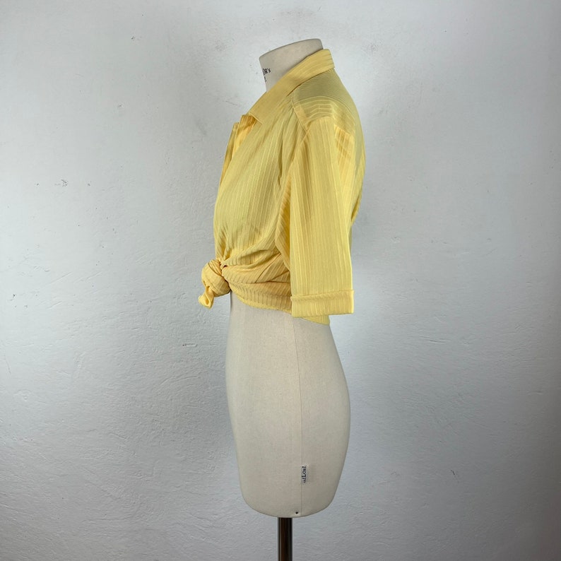May include: A yellow short-sleeved collared shirt with a ribbed texture. The shirt is tied at the waist.