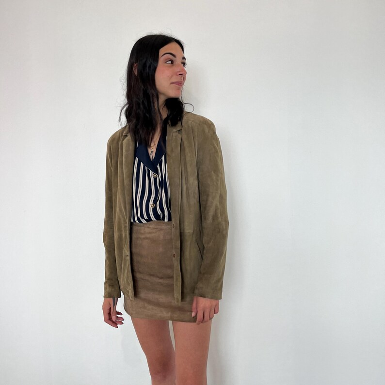May include: A woman wearing a brown suede jacket and a brown suede mini skirt. She is wearing a striped shirt underneath the jacket.