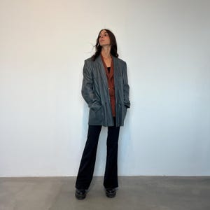 Op de afbeelding: Een donkergrijze leren blazer met een roestkleurig shirt eronder. De blazer heeft een dubbele knoopsluiting en een ontspannen pasvorm.