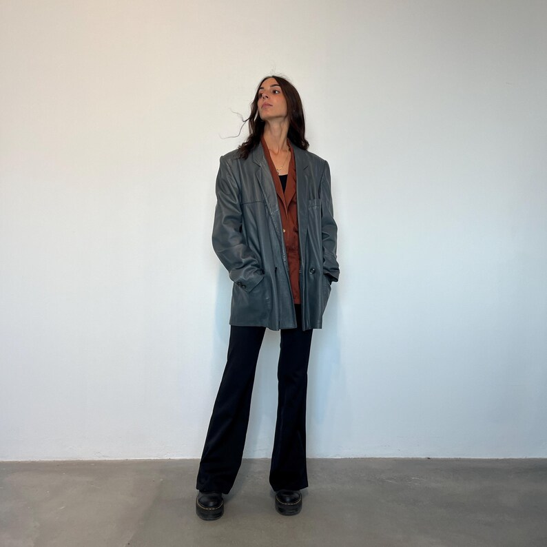 Op de afbeelding: Een donkergrijze leren blazer met een roestkleurig shirt eronder. De blazer heeft een dubbele knoopsluiting en een ontspannen pasvorm.