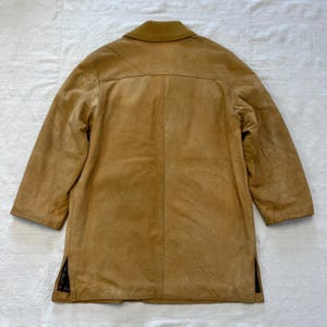 May include: A brown suede jacket with a collar and long sleeves. The jacket has a plaid lining visible at the sides.