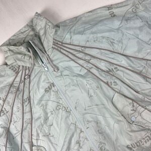 May include: Light blue golf-themed jacket with a full zipper and drawstring hood. The jacket features a repeating pattern of golf players and the word "SUMMER GOLF" in a darker shade of blue. The jacket has a button closure and brown drawstrings.