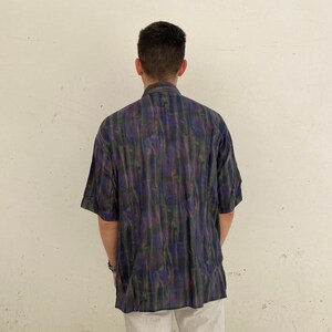 May include: A short-sleeved button-down shirt with a dark blue, green, and purple abstract print.