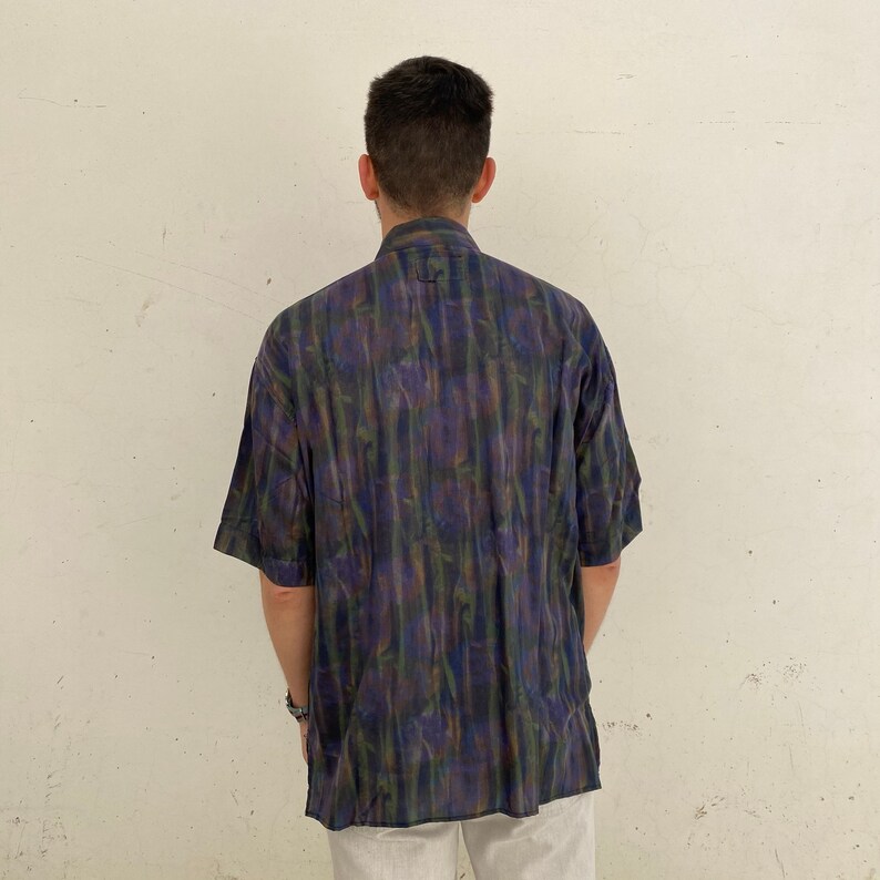 May include: A short-sleeved button-down shirt with a dark blue, green, and purple abstract print.