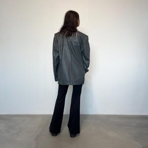 Op de afbeelding: Een donkergrijze blazer met een lange, ontspannen pasvorm. De blazer heeft een simpel ontwerp zonder zichtbare zakken of versieringen. Het model draagt een zwarte flared broek.