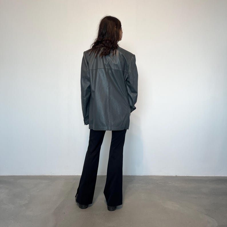 Op de afbeelding: Een donkergrijze blazer met een lange, ontspannen pasvorm. De blazer heeft een simpel ontwerp zonder zichtbare zakken of versieringen. Het model draagt een zwarte flared broek.