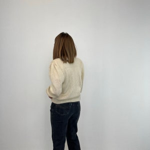 May include: A white fluffy sweater with puffed sleeves and a slightly cropped fit. The sweater is worn over black jeans.