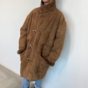 May include: A brown suede coat with a high collar and toggle closures. The coat has a fur lining and two pockets.