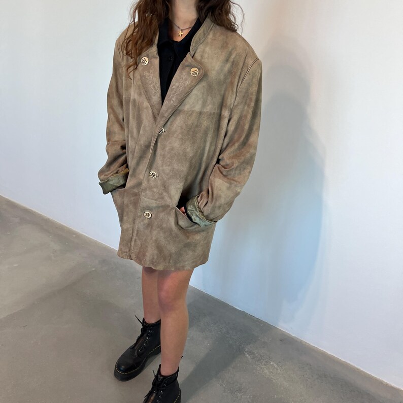 May include: A brown suede jacket with a double-breasted closure and a collar. The jacket has a slightly oversized fit and features a subtle distressed look.