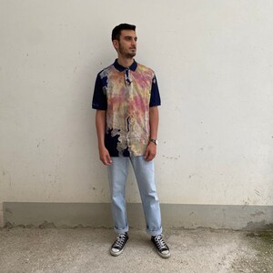 May include: A blue and white tie-dye polo shirt with a button-down collar. The shirt has a relaxed fit and is made of a lightweight fabric.