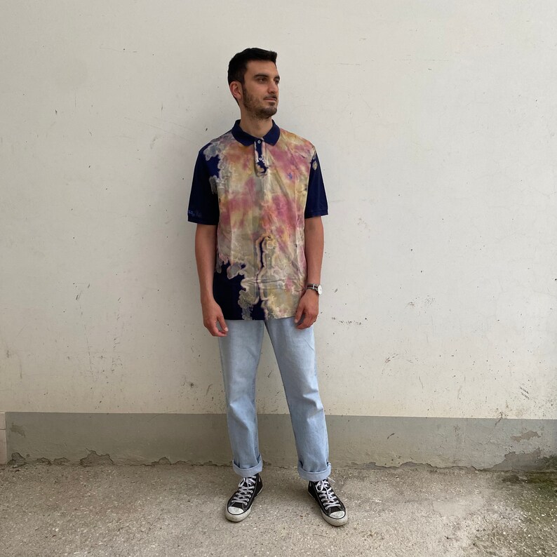 May include: A blue and white tie-dye polo shirt with a button-down collar. The shirt has a relaxed fit and is made of a lightweight fabric.