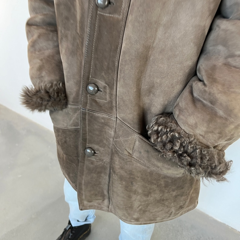 Puede incluir: Una chaqueta de piel de oveja de color marr&oacute;n con cierre de botones y dos bolsillos. La chaqueta tiene un ribete de piel en los pu&ntilde;os y el cuello.