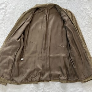 May include: A brown suede jacket with a button closure and a brown satin lining. The jacket is unbuttoned and laid flat.