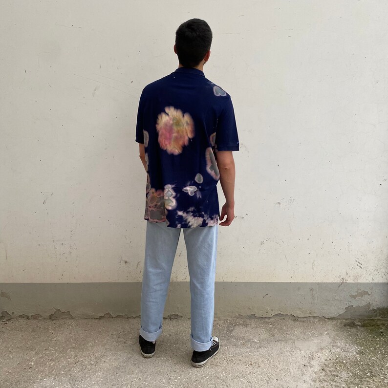 May include: A navy blue short-sleeved shirt with a tie-dye pattern in shades of pink, yellow, and white. The shirt is worn over light blue jeans.