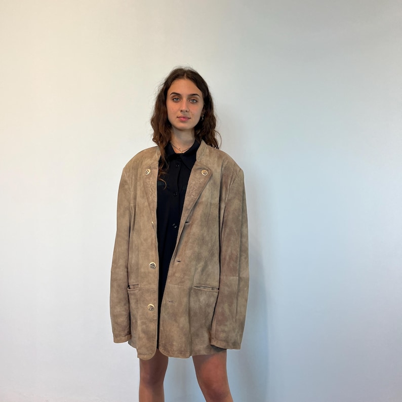 May include: A brown suede jacket with a button closure and two pockets. The jacket has a slightly oversized fit.