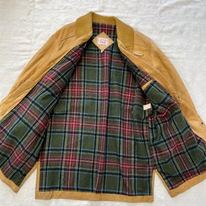 May include: A tan leather jacket with a plaid lining. The jacket has a collar and a button closure. The label inside the jacket reads "Lands' End".