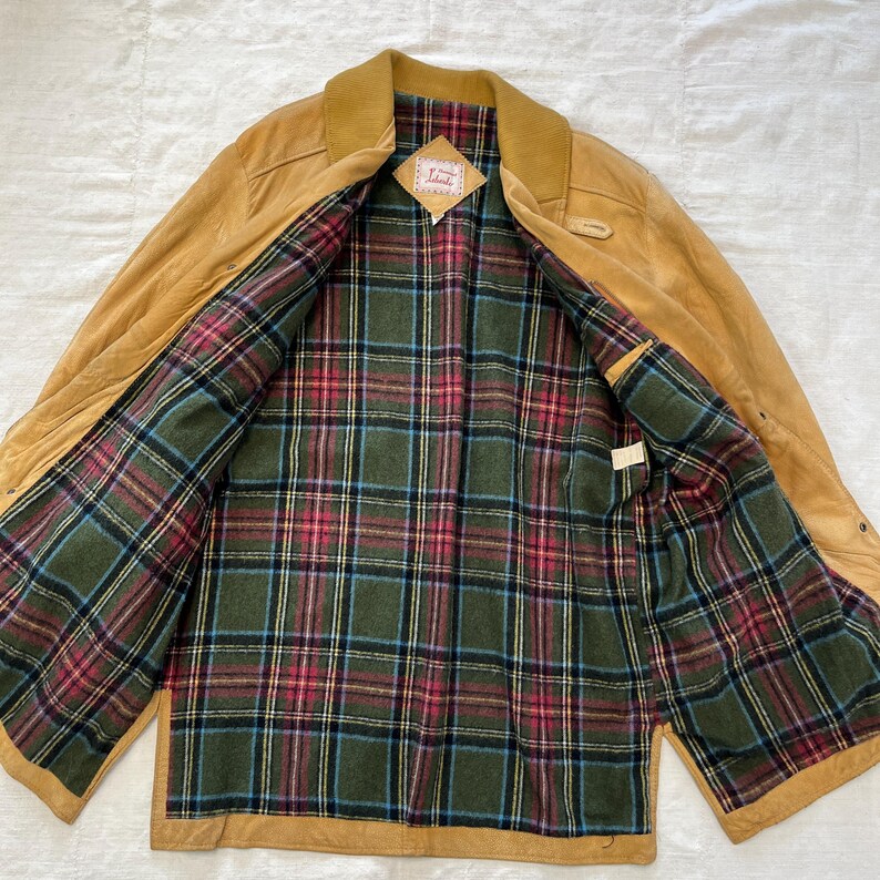 May include: A tan leather jacket with a plaid lining. The jacket has a collar and a button closure. The label inside the jacket reads "Lands' End".