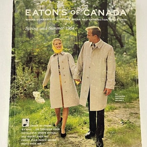 May include: A vintage Eaton's of Canada catalogue cover from Spring and Summer 1964. The cover features a couple walking in a wooded area. The woman is wearing a light-coloured coat and a yellow scarf. The man is wearing a similar coat. The text on the cover reads "Eaton's of Canada" and "Where Guaranteed Shopping Began and Satisfaction Never Ends".