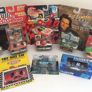 May include: A collection of NASCAR die-cast cars in various packaging. The cars are from different racing series and feature drivers such as Billy Dean, Bill Elliott, and Chase Race. The cars are in a variety of colours, including red, blue, green, and black.