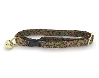 Pode incluir: Uma coleira para gatos estampada com um sino dourado. A coleira apresenta uma fivela de plástico preta e um anel de metal dourado. O tecido tem um design floral nas cores preto, verde, rosa e azul.