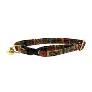 Könnte beinhalten: Ein farbenfrohes Katzenhalsband mit einem geometrischen Muster in Braun-, Orange-, Grün- und Lilatönen. Das Halsband hat eine schwarze Kunststoffschnalle und eine goldene Glocke.