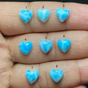 May include: Eight heart-shaped gemstones in shades of light blue and white. Each stone is numbered from one to eight. The gemstones have a smooth, polished finish with a marbled effect. The gemstones are held in a hand.