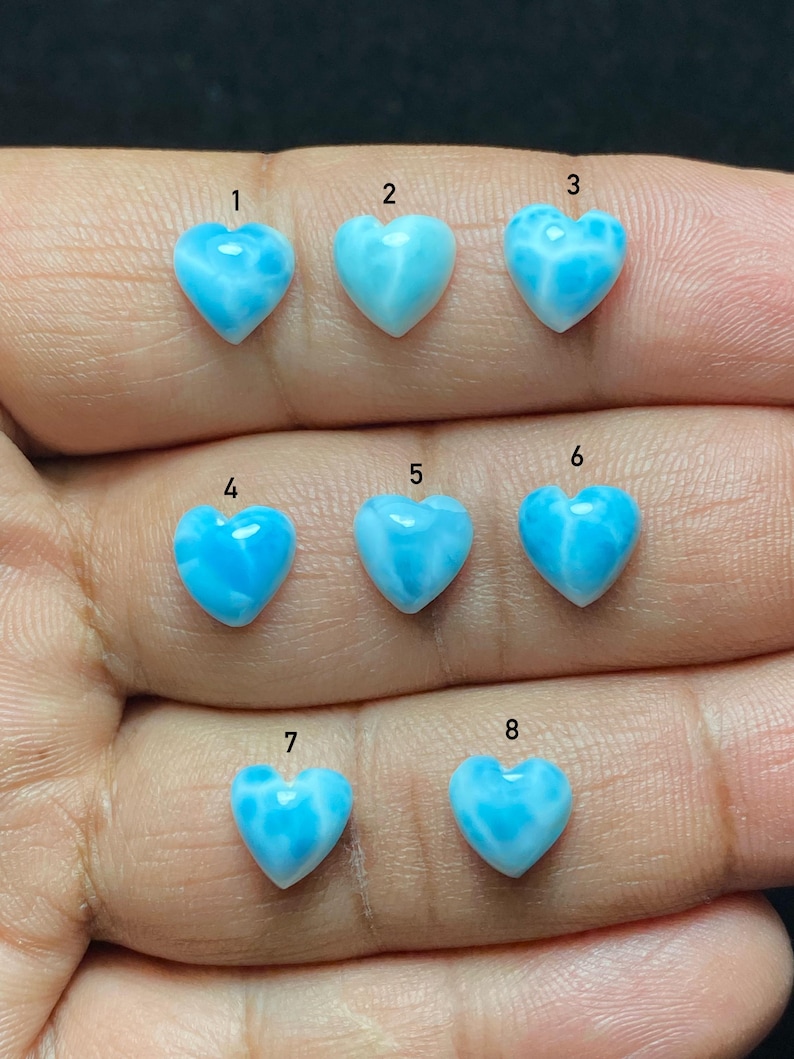 May include: Eight heart-shaped gemstones in shades of light blue and white. Each stone is numbered from one to eight. The gemstones have a smooth, polished finish with a marbled effect. The gemstones are held in a hand.