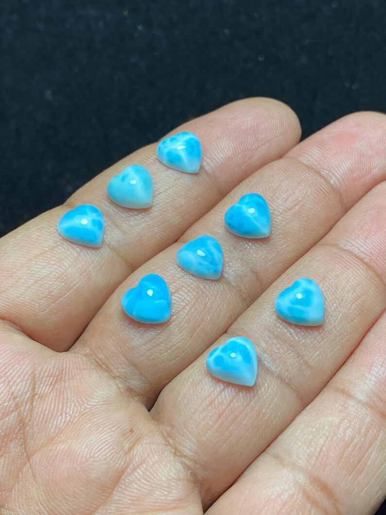 May include: Nine heart-shaped gemstones in shades of blue and white. The polished stones have a marbled effect. The image is a close-up, highlighting the details of the small heart-shaped stones. The gemstones are likely for jewellery making.