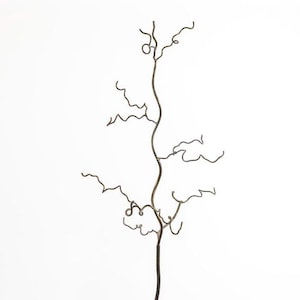 Op de afbeelding: Een metalen sculptuur van een boom met een gedraaid, tak-achtig ontwerp. De sculptuur staat in een pot met groen gras en kleurrijke bloemen.