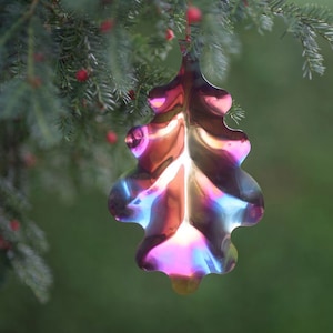Può includere: Un ornamento metallico iridescente a forma di foglia con una texture ondulata, appeso a un ramo d'albero.