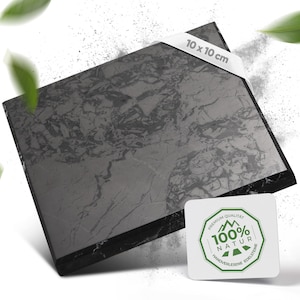Könnte beinhalten: Eine schwarze Marmorfliese mit grauer Maserung. Die Fliese ist 10 cm x 10 cm groß. Ein weißer Aufkleber mit grünem Text lautet "Premium Qualität 100% Natur Handverlesene Edelsteine".