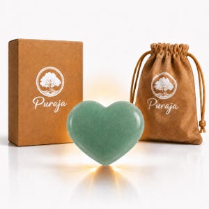 Può includere: Una pietra verde liscia a forma di cuore posizionata tra una scatola di cartone marrone e un sacchetto marrone con coulisse. Sia la scatola che il sacchetto presentano un logo circolare bianco che raffigura un albero sopra la scritta Puraja.