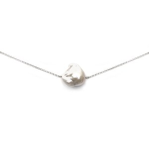 Puede incluir: Un delicado collar con un gran colgante de perla blanca de forma irregular. La perla est&aacute; suspendida de una fina cadena plateada. El collar se muestra sobre un fondo blanco liso, resaltando la forma &uacute;nica de la perla.