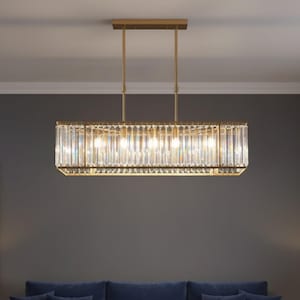 Può includere: Un lampadario rettangolare con cornice color oro e dettagli in cristallo trasparente. L'apparecchio è sospeso al soffitto da due aste color oro. Il lampadario è sopra un divano blu con cuscini abbinati.