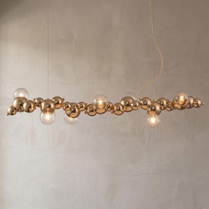 May include: A contemporary gold chandelier with a cluster of spherical lights. The fixture features various sizes of gold spheres and clear glass globes, creating a unique lighting design. The light fixture hangs from a single cord.