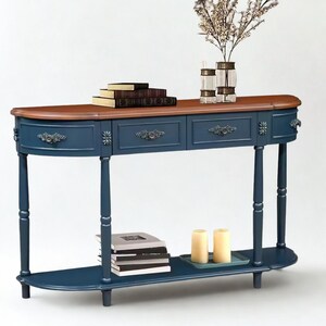 Może przedstawiać: Granatowa konsola z brązowym blatem. Stół posiada dwie szuflady z ozdobnym osprzętem i dolną półkę. Ozdoby to książki, świece i wazon z gałązkami.