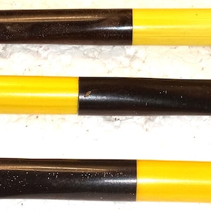 May include: Three cylindrical objects, each with a dark brown end and a bright yellow end. The objects are arranged horizontally against a light-colored background. The yellow sections appear to be made of a smooth, solid material.