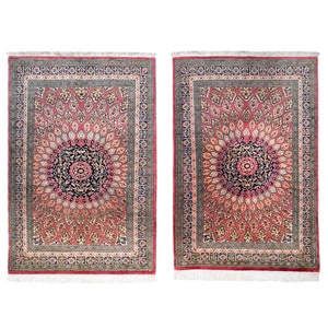 May include: Two rectangular rugs with intricate floral patterns. The rugs feature a central medallion design in navy and pink, surrounded by a field of pink and cream-colored motifs. A border of navy and gray frames the design, with a fringe along the bottom edge.