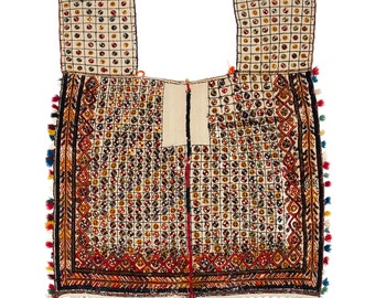 Op de afbeelding: Een traditioneel geborduurd textiel met een geometrisch patroon van cirkels en vierkanten in tinten rood, blauw, geel en groen. Het textiel heeft een franje rand met kwastjes.