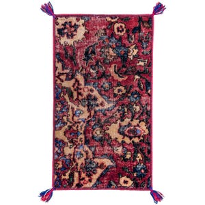 May include: A rectangular, distressed-look rug with a deep red background and a faded floral pattern in beige and blue. The rug has a magenta border and tassels in blue, red, and white at each corner. The rug's dimensions are not visible.