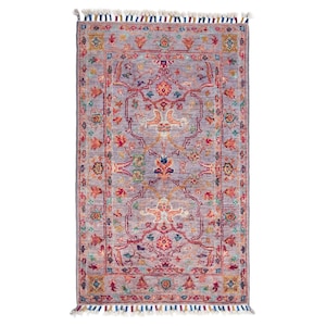 Könnte beinhalten: Ein rechteckiger Teppich mit einem zentralen Medaillon-Design in den Farbtönen Lavendel, Rot, Orange und Türkis. Der Teppich hat einen Fransenrand mit Quasten in verschiedenen Farben. Das komplizierte Muster erinnert an traditionelle Orientteppiche.