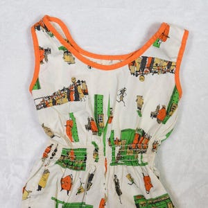 May include: A vintage romper featuring a white background with a colorful city scene print. The sleeveless romper has orange trim and a gathered waist. The print includes green buildings, orange figures, and yellow accents.