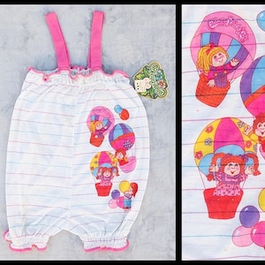 May include: White and pink striped baby romper with pink straps and ruffled edges. The romper features colorful illustrations of Cabbage Patch Kids in hot air balloons. A vintage collectible.