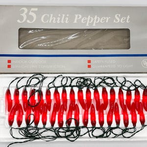 May include: A set of 35 red chili pepper-shaped string lights with green wiring, displayed in a white box. The box is labeled "35 Chili Pepper Set" and includes text indicating indoor/outdoor use and safety features.