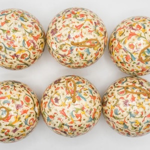May include: A set of six spherical ornaments featuring a cream-colored base with a repeating multi-colored floral and vine pattern in shades of red, blue, yellow, and green. Each ornament includes a small gold-toned cord loop for hanging purposes.