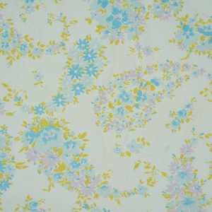 May include: White fabric with a repeating floral pattern. The design features clusters of blue, yellow, and lavender flowers with green leaves. The flowers are scattered across the fabric.