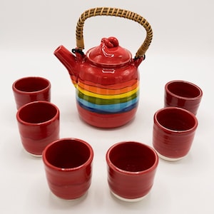 May include: A red ceramic teapot with a rainbow stripe design and a woven handle, along with six matching red teacups.