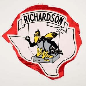 May include: A red and white fabric patch shaped like the state of Texas featuring the text RICHARDSON on a banner. The graphic depicts two black birds with yellow beaks and feet interacting with a grey radio console and a handheld device.