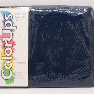 May include: A navy blue extra long twin fitted sheet, packaged in clear plastic. The label on the sheet reads "ColorUps" in a rainbow gradient font, with the text "Extra Long Twin Fitted Sheet" and "by Springmaid". The sheet is made of 60% cotton and 40% polyester.