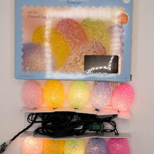 May include: A set of 10 crystal egg lights in a variety of colors, including pink, yellow, and purple. The lights are strung on a black wire and come in a light blue box with the text "COTTONTALE Collection" and "Crystal Egg Light Set".